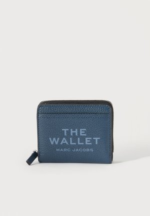 Portefeuille en cuir texturé bleu foncé avec fermeture éclair et texte embossé "THE WALLET MARC JACOBS" sur le devant.
