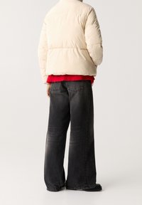 Puffjakke i off-white, rød sweater underneath og oversized sorte jeans med en falmet finish og brede ben. Flade sorte sko.
