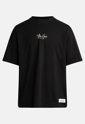 T-shirt nera a maniche corte in cotone. Presenta un piccolo logo bianco sul petto e un'etichetta rettangolare in basso a destra.