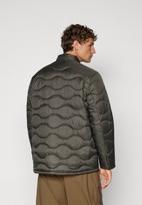 Chaqueta acolchada verde oscura con collar, que presenta un patrón de olas y una textura suave, diseñada para mantener el calor y ofrecer comodidad.