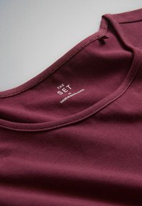 Maroon crew neck shirt with printed label "THE SET M MADE IN BANGLADESH" inside the collar area.