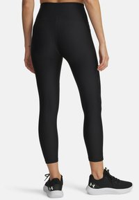 Leggings negros de talle alto con una tela suave y elástica, que presentan un acento lateral y se combinan con zapatillas deportivas negras con suelas blancas.