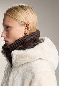 Hvid faux fur hættejakke med en tyk, ribbet brun strikkrave. Har lynlåslukning og blød tekstur, der fremhæver de kontrasterende farver.