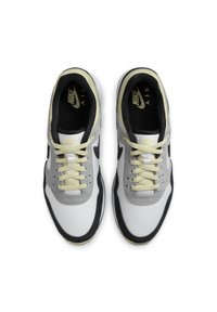 Zapatillas Nike con una parte superior blanca y superposiciones grises, acentos negros y una suela amarilla. El diseño incluye cordones planos y un collar acolchado.