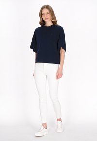 T-shirt oversize blu navy a maniche corte, abbinato a pantaloni bianchi slim-fit e sneakers bianche. Design semplice con una vestibilità rilassata.