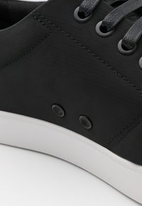 Czarne sneakersy z teksturowaną cholewką, wyposażone w szare sznurówki, dwa otwory na sznurówki i białą gumową podeszwę. Gładkie wykończenie z delikatnymi detalami przeszycia.