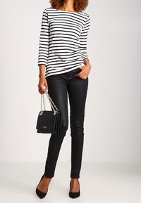 Svartvitrandig långärmad topp, smala svarta jeans, svarta klackar och en quiltad svart handväska med en silverkedja som axelrem.