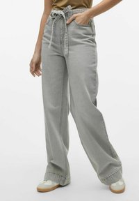 Vaqueros de pierna ancha de color gris claro con una cintura con cinturón, con un ajuste holgado y bolsillos frontales, combinados con zapatillas blancas y crema.