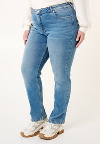 Jean droit bleu clair en denim, avec une taille mi-haute, des poches avant et un design minimaliste. Orné de détails de couture.