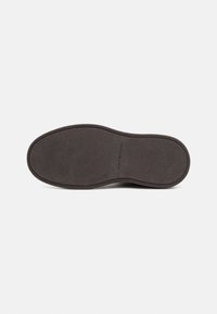 Semelle de chaussure en caoutchouc foncé avec surface texturée, bords incurvés et empreinte de logo au centre. Matériau lisse et durable.
