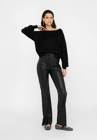 Schwarzer übergroßer Strickpullover mit subtiler Textur, kombiniert mit hochtaillierter schwarzer Kunstleder-Hose mit Schlag und gemusterten Ballerinas.