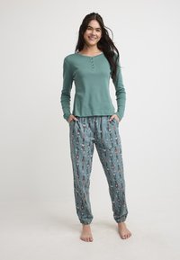 Lichtblauwe longsleeve top met een gestructureerd patroon en knopen, gecombineerd met losse pyjamabroeken met een speelse notenkrakerprint.