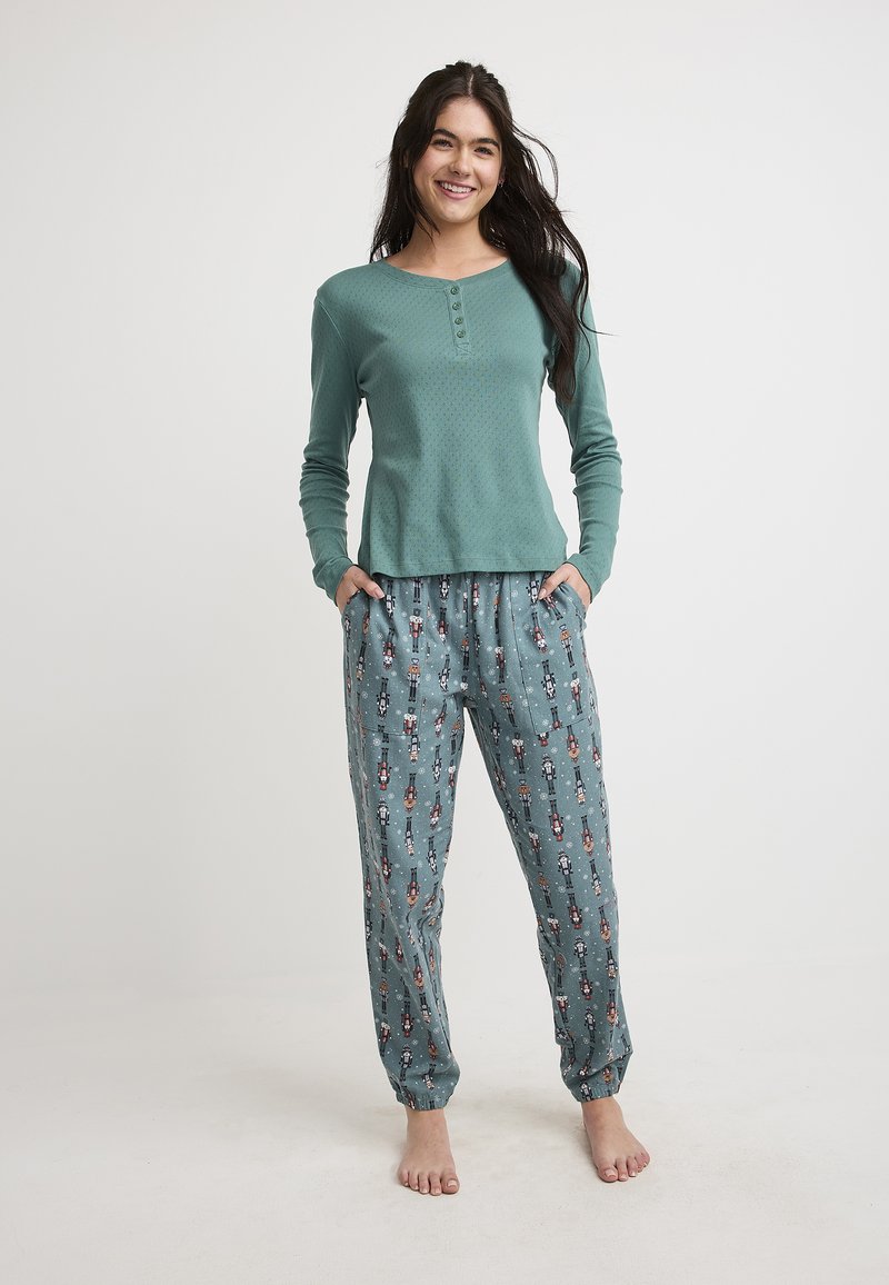 Lichtblauwe longsleeve top met een gestructureerd patroon en knopen, gecombineerd met losse pyjamabroeken met een speelse notenkrakerprint.