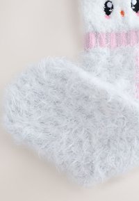 Calzino bianco soffice con una superficie testurizzata e pelosa. Presenta un polsino a coste rosa e un motivo decorativo di un volto animale nella parte superiore.