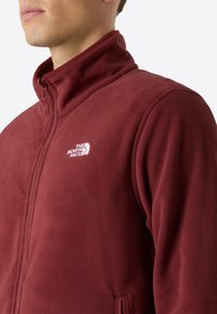 Giacca in pile bordeaux con colletto alto, zip frontale e logo sul petto sinistro. Texture morbida con tasche laterali. Finissaggio in tessuto liscio.