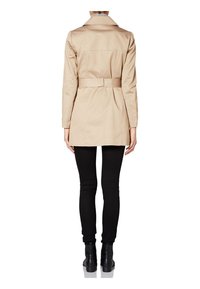 Béžový trenčkot s opaskem v pase, dlouhými rukávy a klasickým límcem, zkombinovaný s černými slim-fit kalhotami a kotníkovými botami.