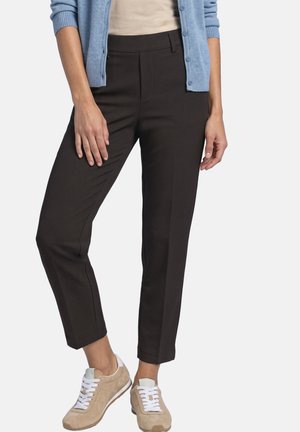 Kvinde iført smalle sorte ankellange bukser, beige sneakers med hvide snørebånd, en beige top og en lyseblå cardigan med knapper.