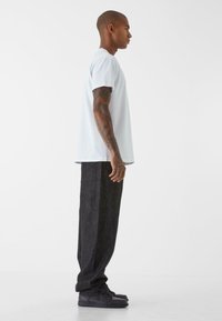 T-shirt di cotone azzurro chiaro abbinato a pantaloni in denim scuri e comodi. Presenta maniche corte e una silhouette dritta, indossato con sneakers nere.