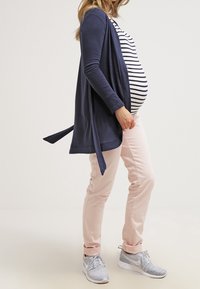 Mörkblå cardigan över randig topp, tillsammans med ljusrosa byxor och grå sneakers. Cardigan har en knytdetalj; byxorna är rakskurna.