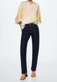 Blusa de patrón paisley claro con mangas de tres cuartos, combinada con jeans rectos de color azul oscuro y sandalias de tacón marrones.