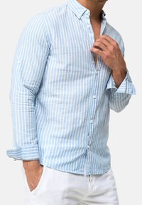 Camisa de rayas azul claro hecha de tela con una textura suave. Cuenta con cuello abotonado, botones frontales completos y mangas remangadas con detalle en contraste.