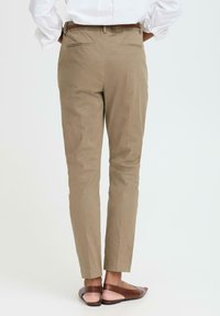 Bežové kalhoty na míru s hladkým texturem, slim fit a zadními kapsami. Nosit s hnědými nazouvacími botami na světlém pozadí.