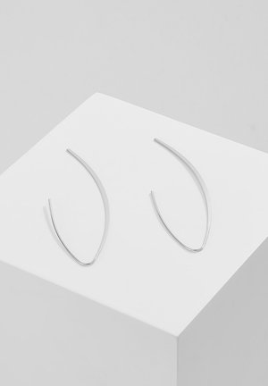 Zilveren metalen oorbellen met langwerpige, gebogen vormen en een gladde textuur. Weergegeven op een witte standaard, wat het minimalistische ontwerp benadrukt.