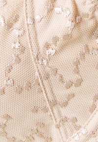 Μπεζ υφασμάτινη επιφάνεια με υφή, που διαθέτει κεντημένα σχέδια σε κρέμα χρώμα, με όψη υφασμένου πλέγματος και ορατές γραμμές ραψίματος στο σχέδιο.