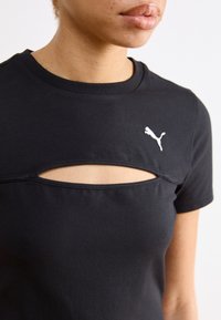 Juoda medvilninė marškinėliai su priekyje esančia išpjova ir trumpomis rankovėmis, viršutiniame kairiajame kampe yra mažas baltas Puma logotipas.