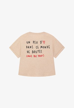 T-shirt beige à manches courtes avec un design textuel noir et rouge. La phrase indique : "Un peu d'amour dans ce monde de brutes (mais pas trop)."