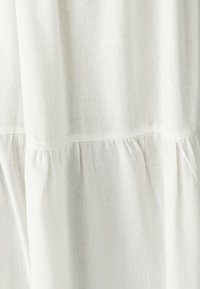 Bijela platnena tkanina s blago teksturiranom površinom, koja na rubu ima nabrane nabore za dodatnu detaljnost.