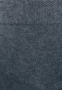Graue Baumwollsocke mit gerippter Textur. Der obere Teil ist feiner gestrickt und geht an der Basis in ein dickeres, strukturierteres Gewebe über.