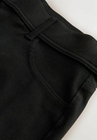 Material denim negru cu o textură fină, având o talie cusută, buclă pentru curea și un design cu buzunar lateral.