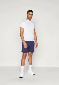 White short-sleeve t-shirt paired with navy shorts. Model stands with hands relaxed, wearing white sneakers and crew-length socks.
