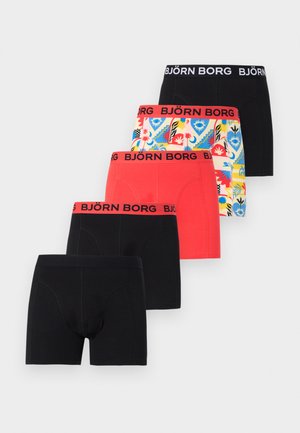 Férfi modell áll mezítláb egy fehér fal előtt, élénk kék Björn Borg boxeralsót viselve, kissé oldalra nézve.