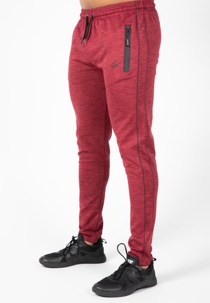 Rode heathered sportbroeken hebben een slim fit, elastische tailleband, een trekkoord, een ritssluiting zijzak en zwarte accenten aan de zijkant. Gecombineerd met zwarte sneakers.
