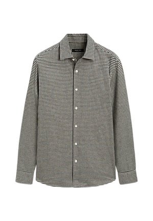 Chemise à carreaux noirs et blancs avec manches longues, col et boutons blancs. Tissu doux, ourlet droit et coupe régulière.