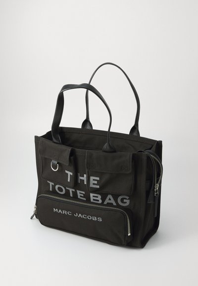 Geantă de tote din pânză neagră, cu două mânere din piele, buzunare frontale, fermoar argintiu și inscripția "THE TOTE BAG MARC JACOBS" imprimată în alb.