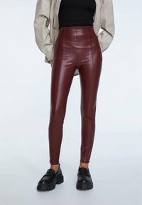 Leggings in ecopelle bordeaux a vita alta, con una trama liscia, forma aderente, cuciture laterali, abbinati a mocassini neri chunky.