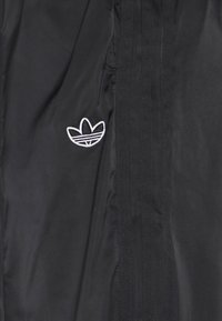 Svart tyg med tre vertikala ränder och en vit Adidas trefoil-logotyp broderad på vänster sida.