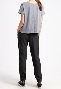 Szary top z krótkim rękawem o luźnym kroju z detalem szwu z tyłu, w połączeniu z czarnymi zwężanymi spodniami z elastycznymi mankietami i bocznymi kieszeniami.