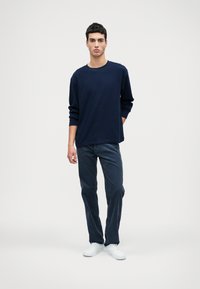 Námornícka dlhá rukávová košeľa, uvoľnený strih, bavlnený materiál. Spárovaná s tmavými džínami a bielymi teniskami, minimalistický dizajn, hladká textúra.