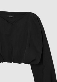 Top nero corto con scollatura a V, maniche lunghe e texture arricciata in vita. L'etichetta riporta "CALLIOPE."