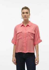 Camicia a maniche corte di colore corallo realizzata in tessuto leggero, con apertura a bottoni, due tasche sul petto e maniche arrotolate.