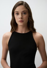 Zwarte geribde tanktop met hoge hals en mouwloos ontwerp, met een gladde textuur en een aansluitende pasvorm.
