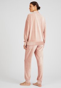 Conjunto de loungewear de terciopelo rosa, que incluye una blusa de manga larga con collar y puños elásticos, acompañada de joggers a juego con tobillos acanalados.