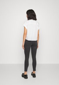 Witte cropped shirt met opgerolde mouwen, gecombineerd met donkergrijze slim-fit jeans en zwarte schoenen. Eenvoudig ontwerp, gladde stoftextuur.