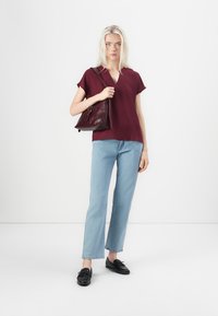 Burgundijas īsām piedurknēm tops, gaiši zilas taisnas kājas džinsi un melni loaferi. Modelis nēsā tumši sarkanu rokassomu, fona ir vienkāršs.