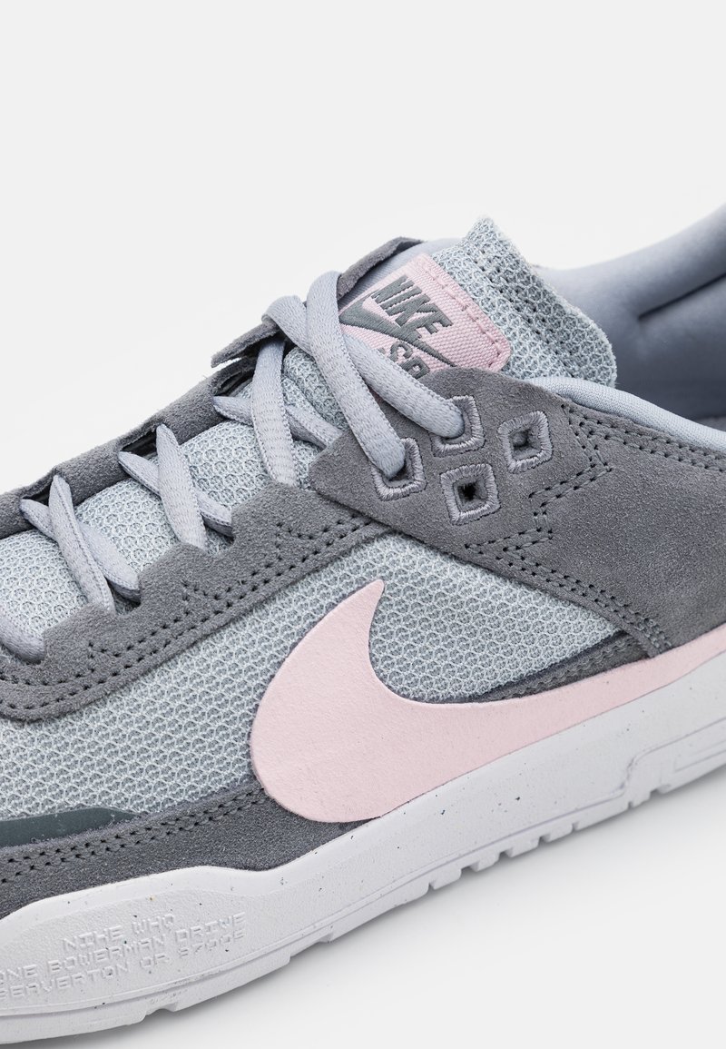 Sneaker Nike avec une tige en maille grise et des accents en daim rose, une semelle extérieure texturée grise et des lacets gris clair.