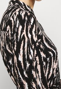 Svart och rosa mönstrad blus med en vågformad design, prydd med ett strukturerat tyg och en krage.